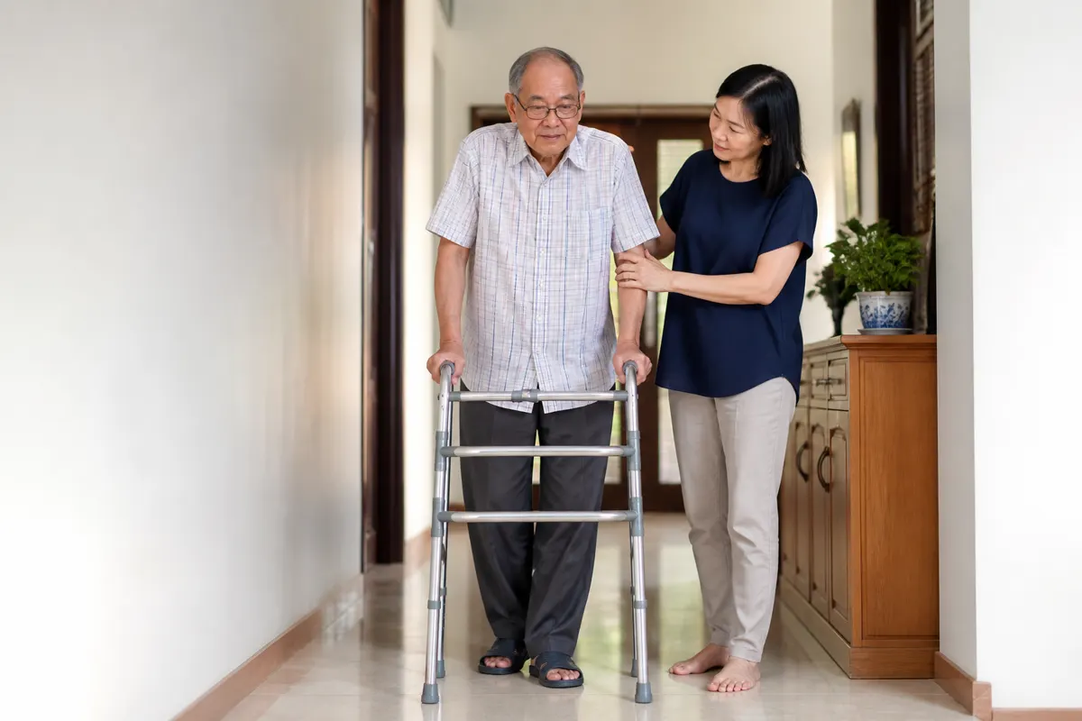 An older Chinese Malaysian man practising safe walking with caregiver support.